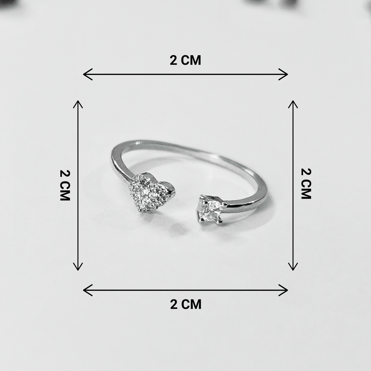 Silver ring with heart-shaped gemstones and measurement markings on a light gray background
