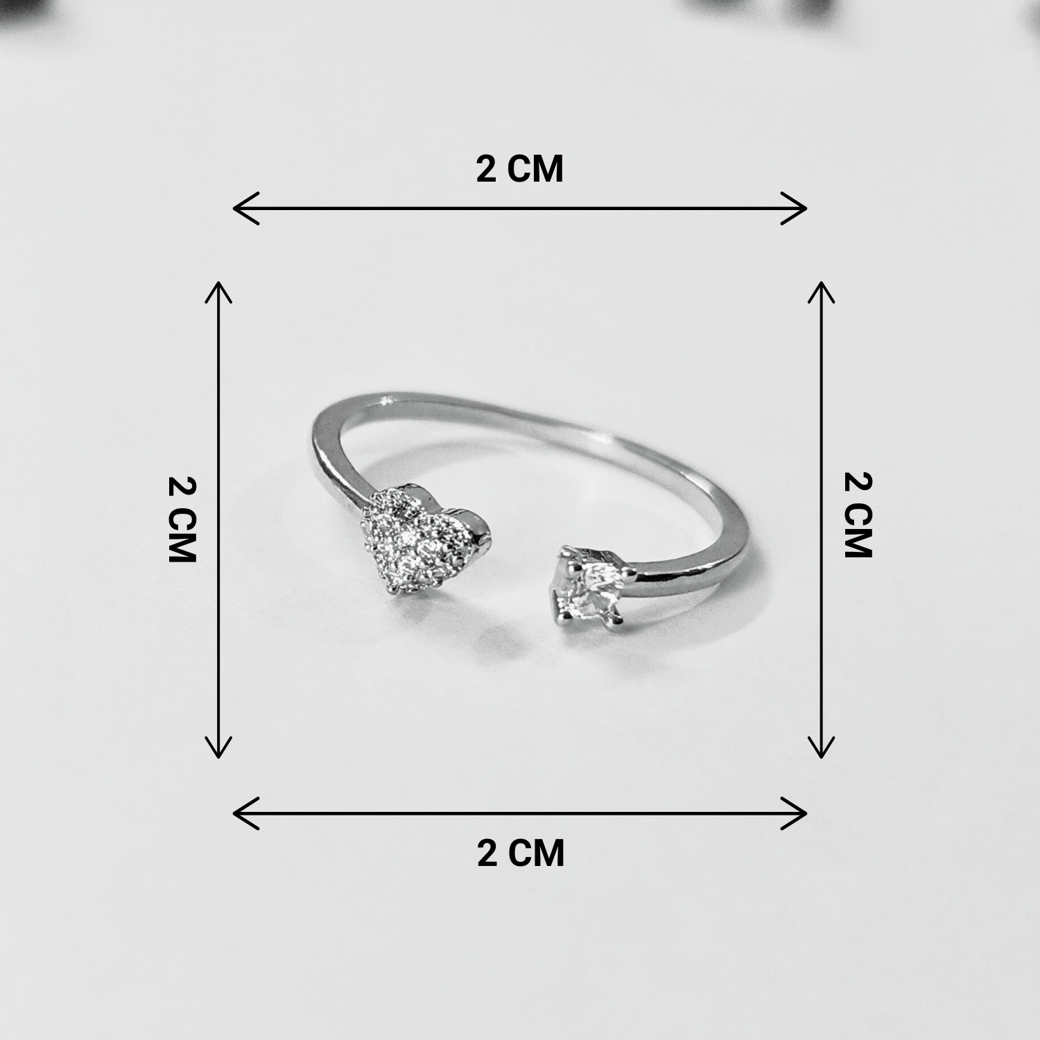 Silver ring with heart-shaped gemstones and measurement markings on a light gray background