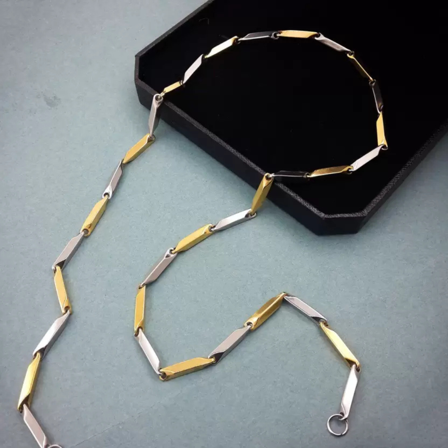 Gold and silver necklace on a green surface with a black box in the background