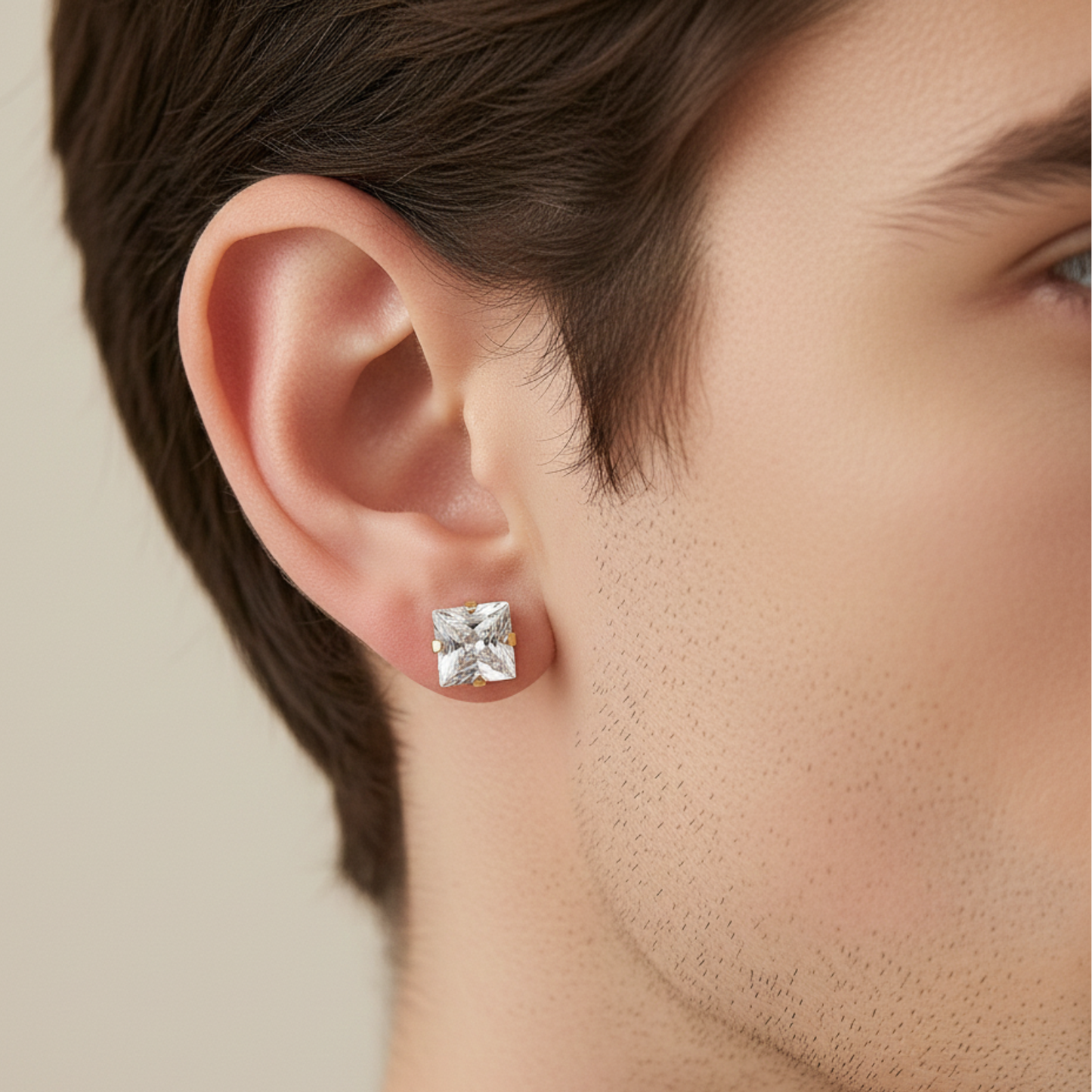 Close-up of a person wearing a square-cut diamond earring on a neutral background