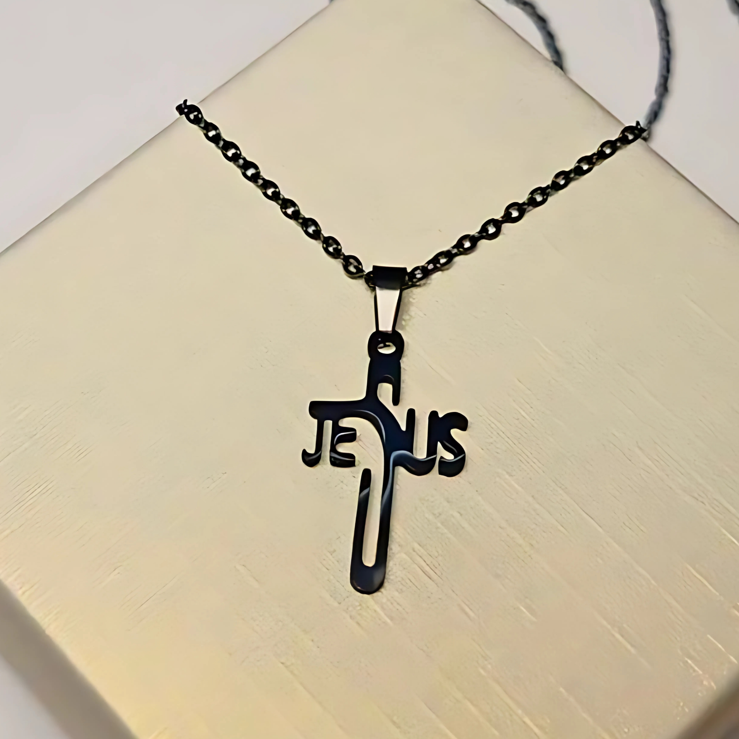 Black 'Jesus' cross necklace on a beige surface