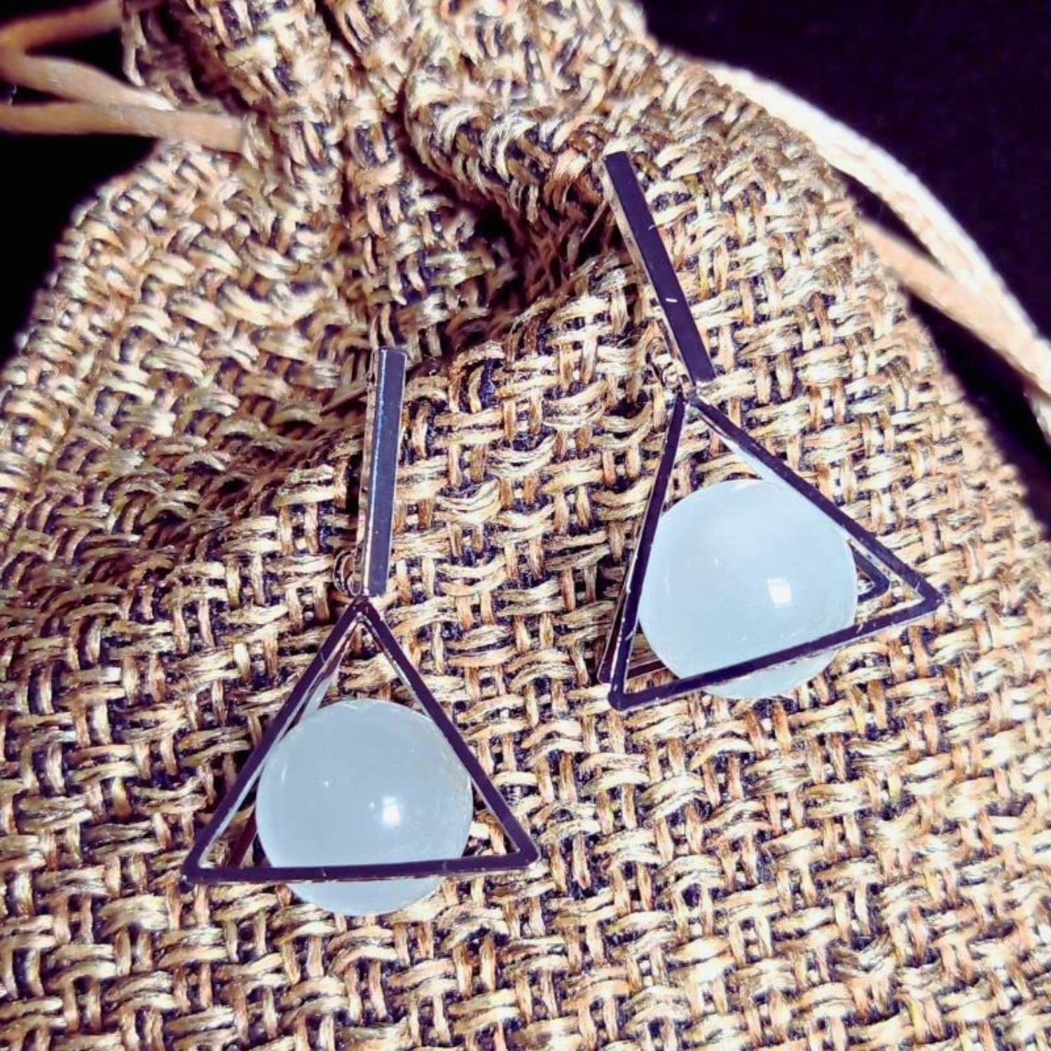 Triangle-shaped earrings with light blue stones on a textured fabric background
