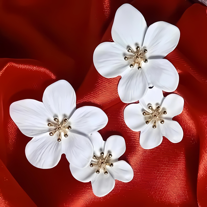 White floral earrings with gold centers on a red fabric background