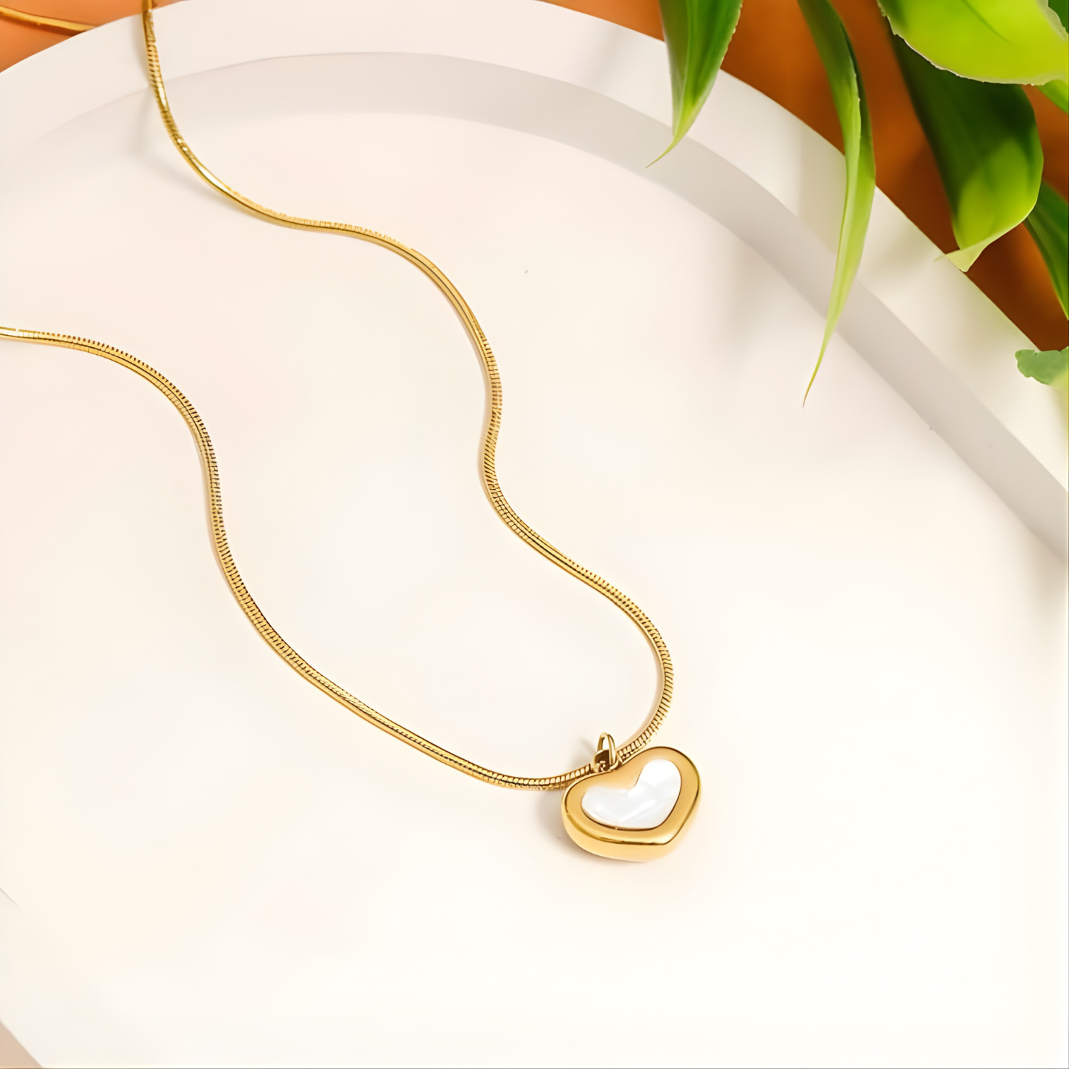 Gold heart-shaped pendant necklace on a white surface with a plant in the background