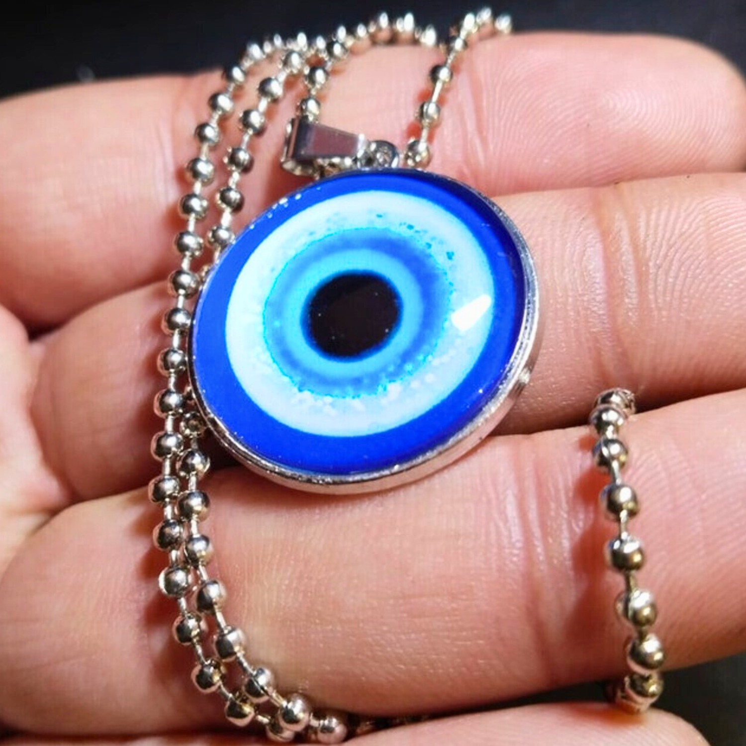 Blue evil eye pendant on a chain held between fingers