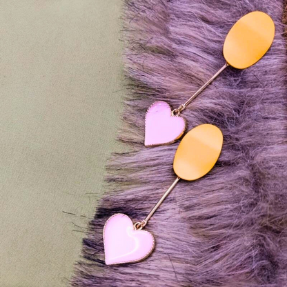 Pair of earrings with pink heart and yellow oval charms on a textured surface.