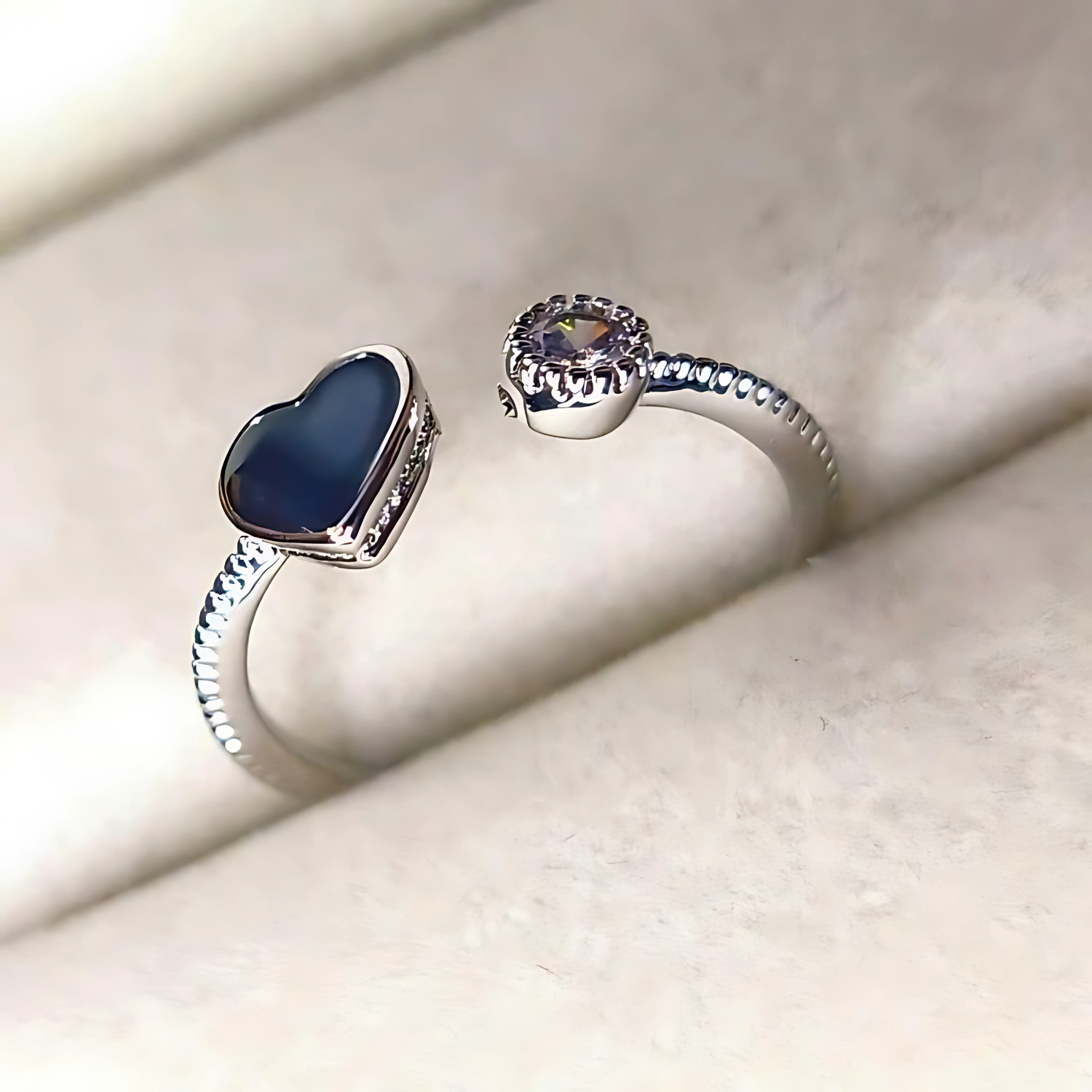 Two silver rings with blue and clear gemstones on a light beige surface