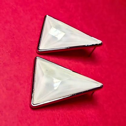 Two triangular earrings with a reflective surface on a red background