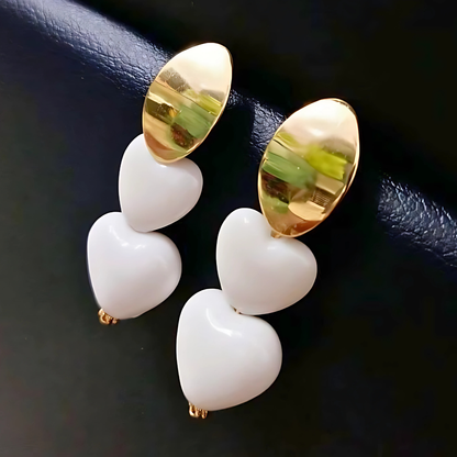 Pair of earrings with gold and white heart-shaped stones on a dark background