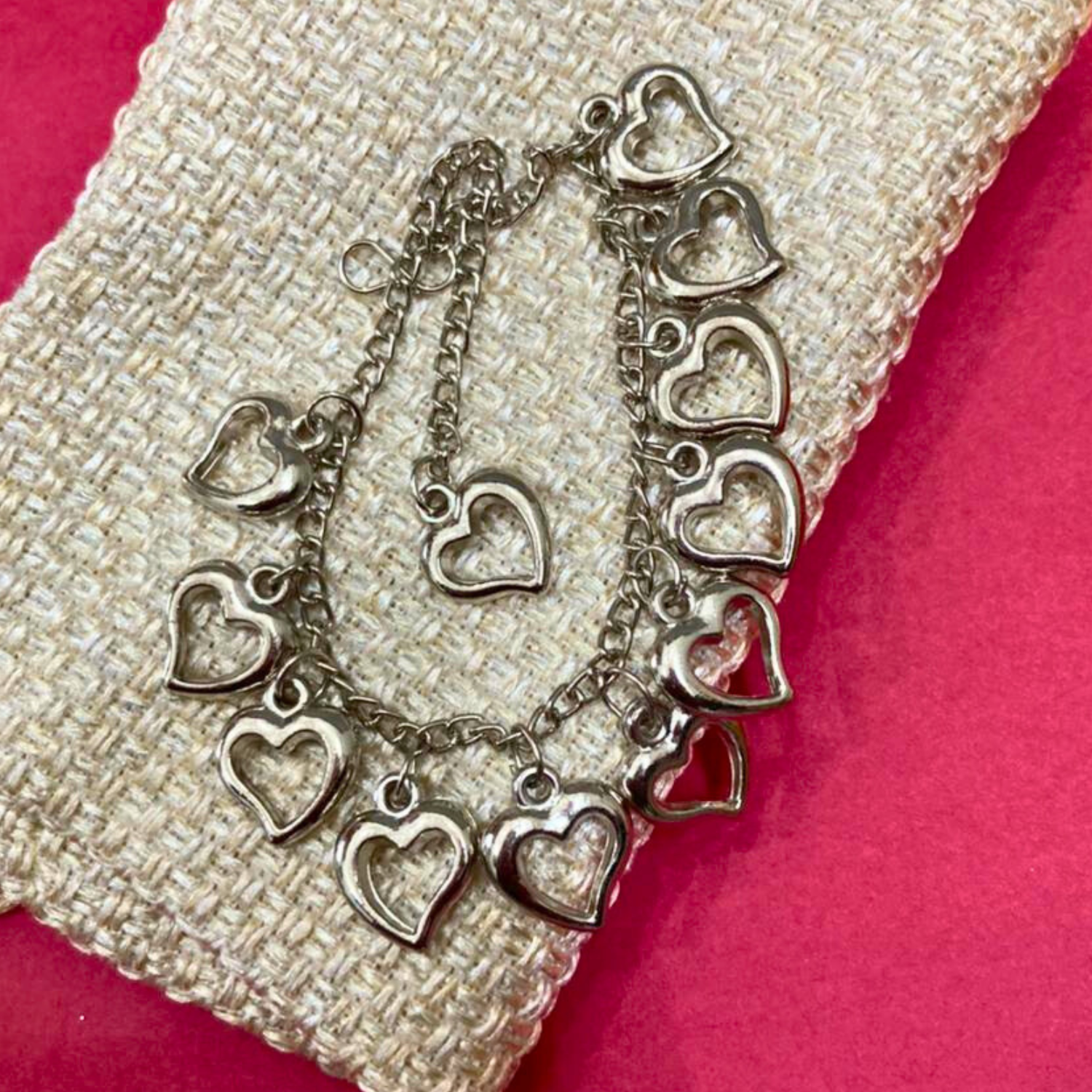 Silver heart-shaped bracelet on a textured surface with a pink background