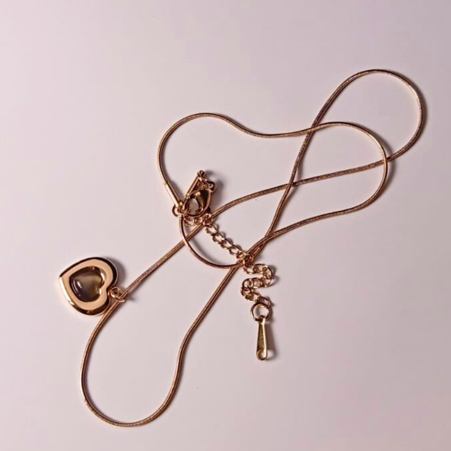 Gold necklace with a heart-shaped pendant on a light pink background