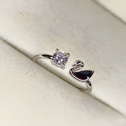 Silver ring with a diamond and a swan design on a light beige background