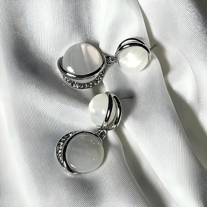 Pair of silver earrings with white stones on a white fabric background