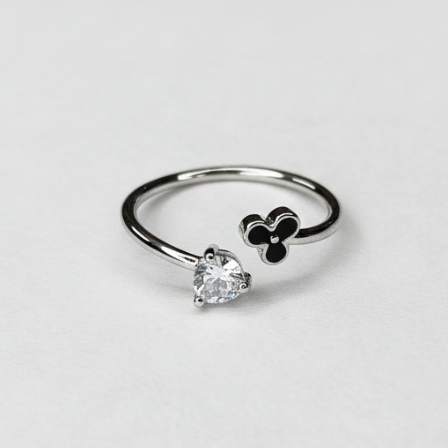 Silver ring with heart-shaped gemstone and black clover design on a light gray background