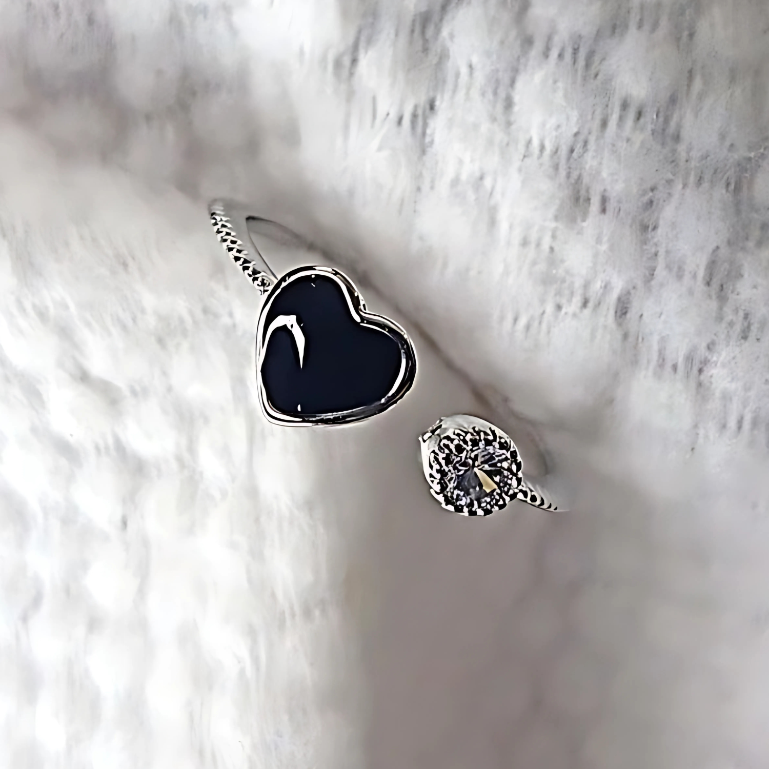 Silver ring with black heart-shaped stone on a textured white surface