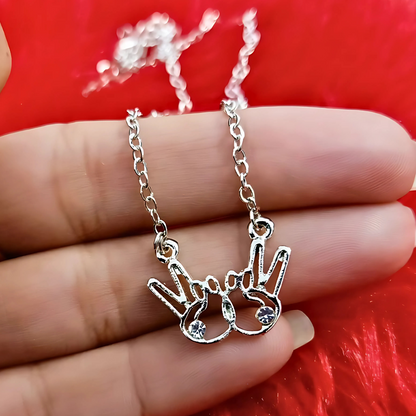 Silver necklace with a hand-shaped pendant held between fingers against a red background