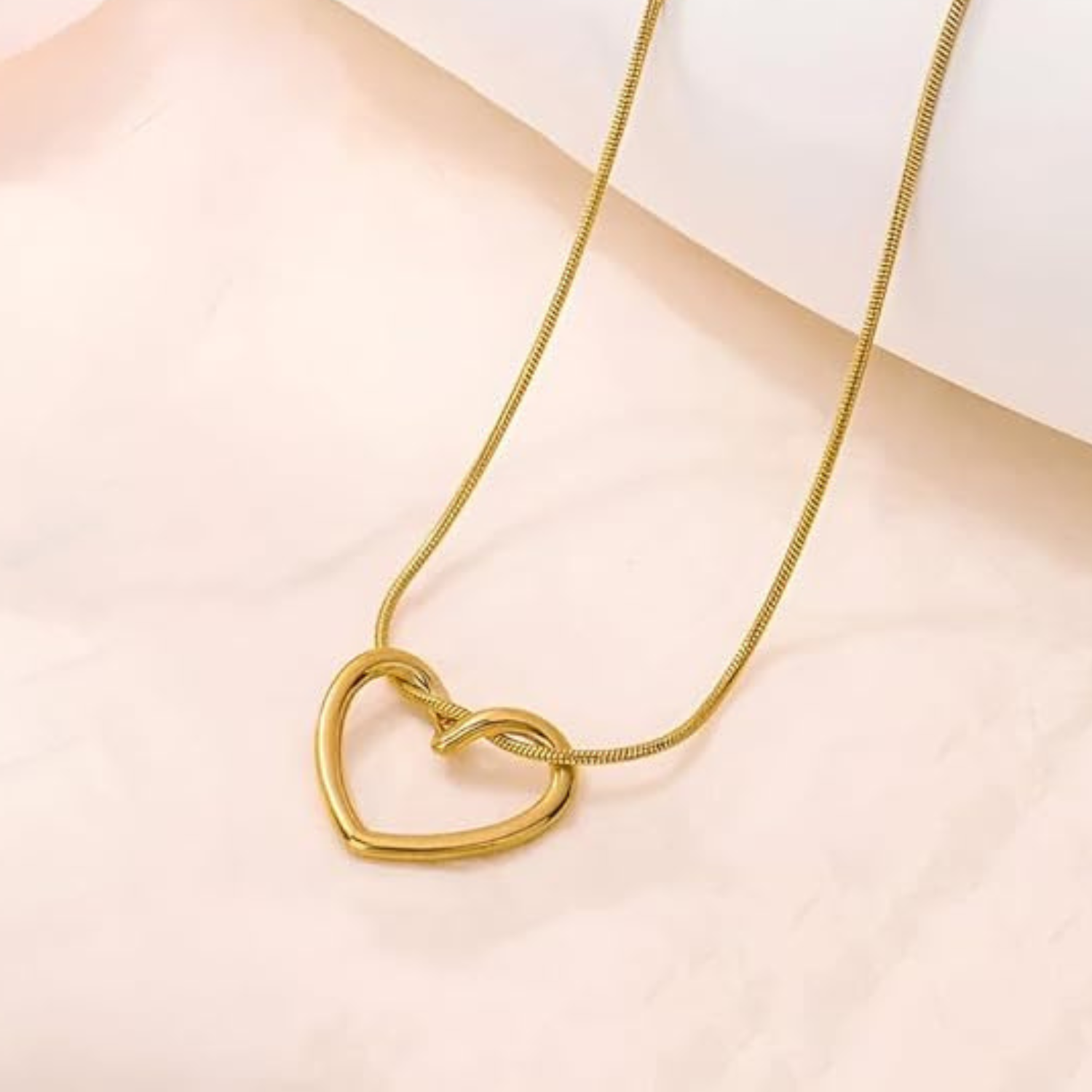 Gold heart-shaped necklace on a light pink background