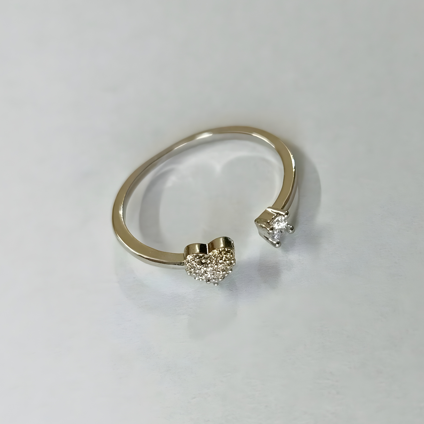 Silver open ring with heart-shaped and round diamond-like embellishments on a light gray background