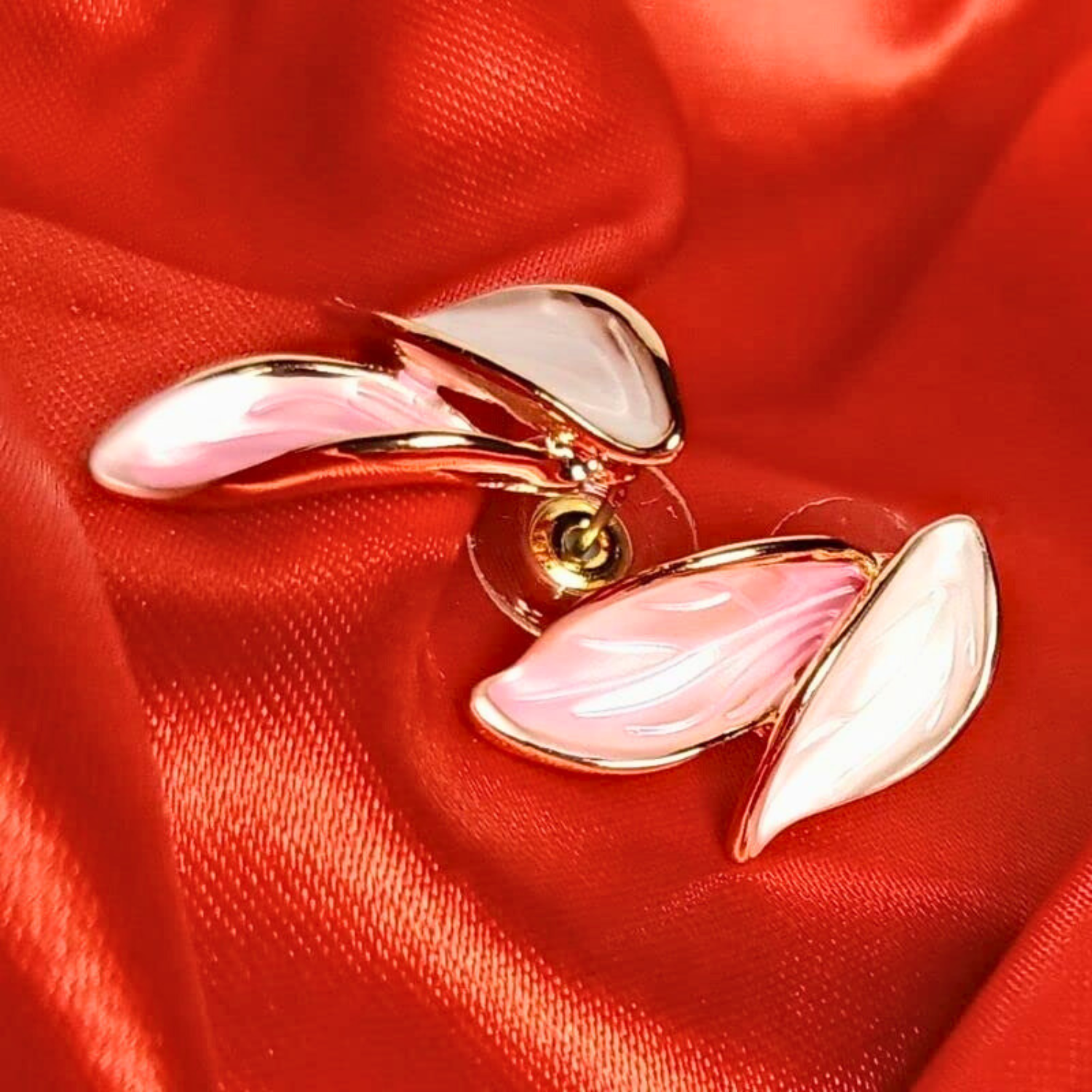 Pink and gold leaf-shaped earrings on red fabric