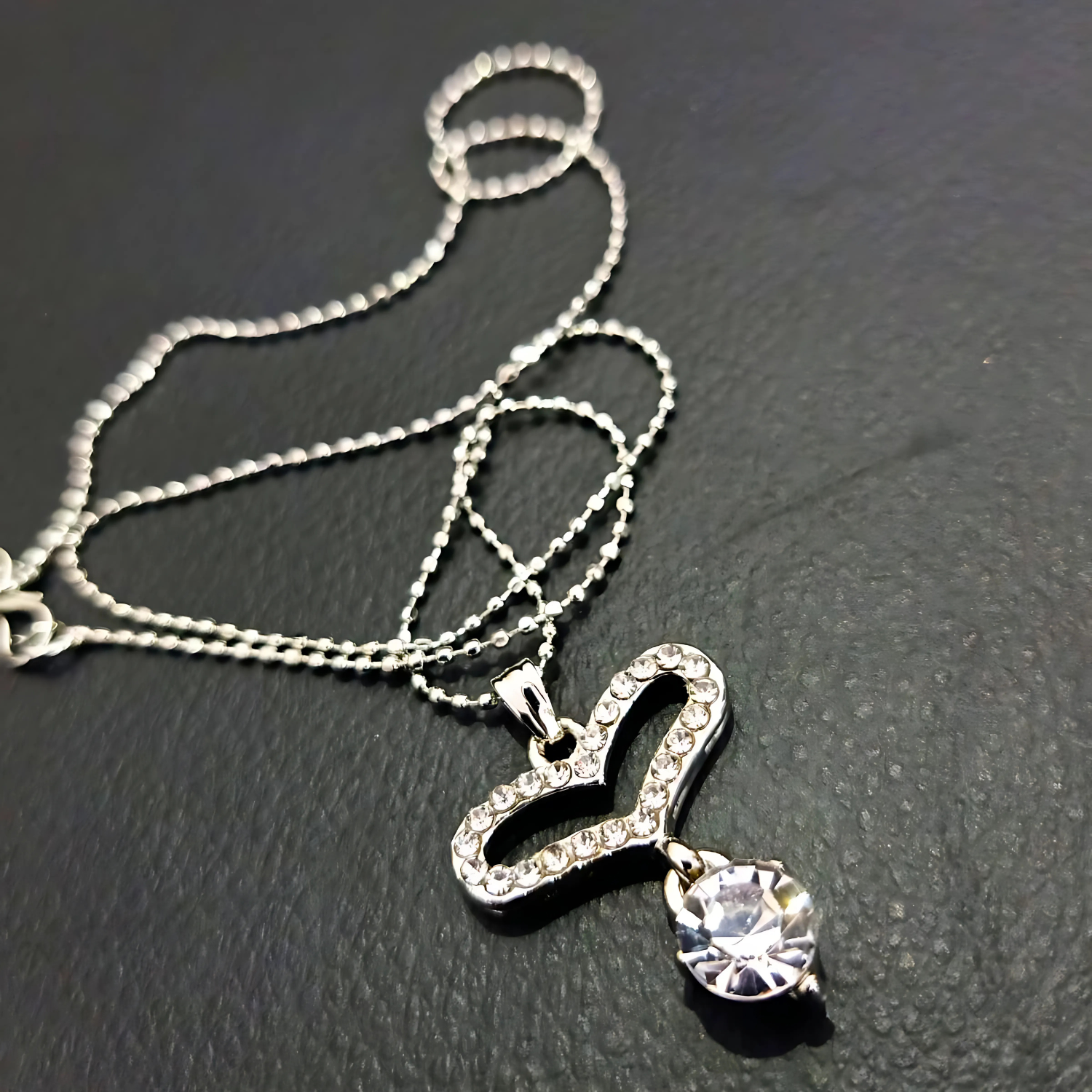 Silver necklace with a heart-shaped pendant on a dark surface