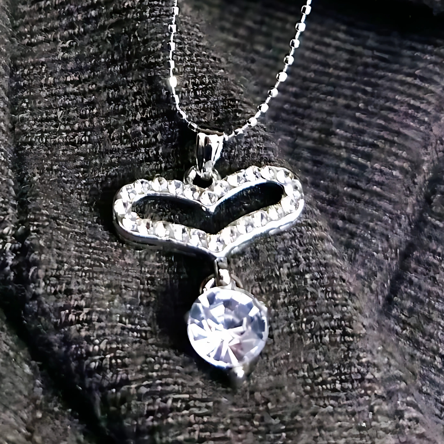 Heart-shaped necklace with a clear gemstone on a textured black background