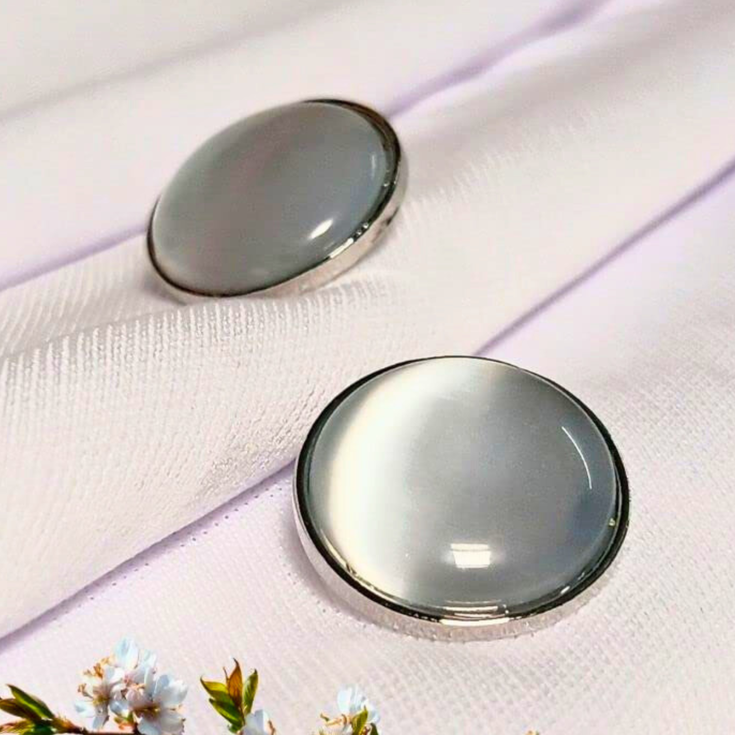 Two round, silver-framed glass objects on a white fabric background with floral elements.