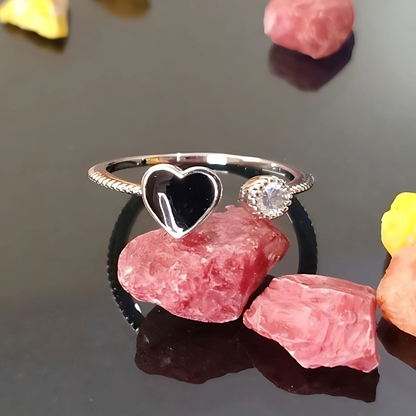 Silver ring with a heart-shaped gemstone on a dark surface with pink stones