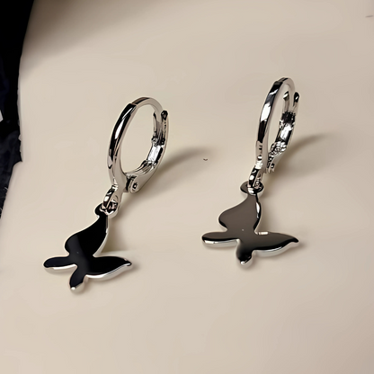 Silver earrings with whale tail designs on a beige background