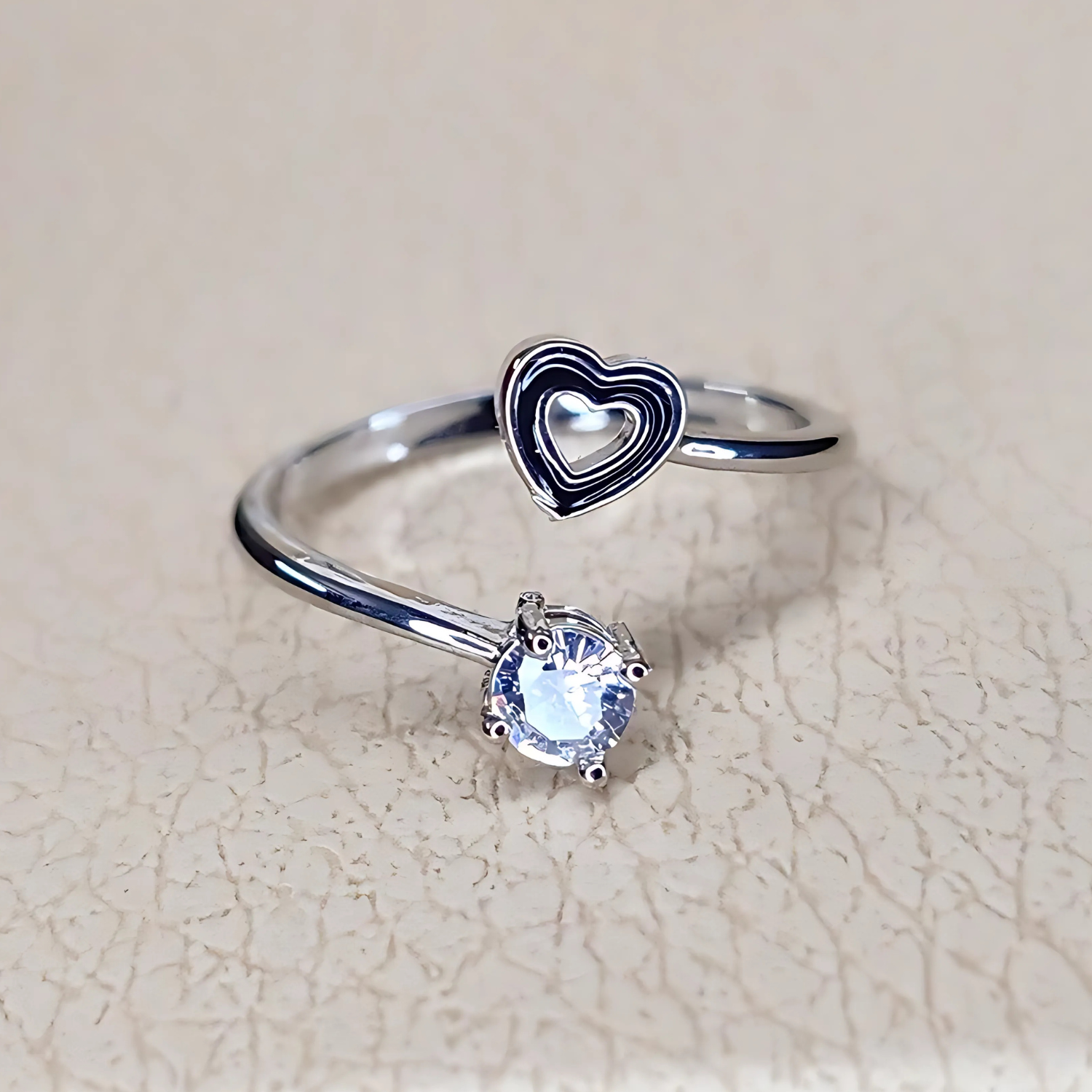 Silver ring with heart design and gemstone on a beige background