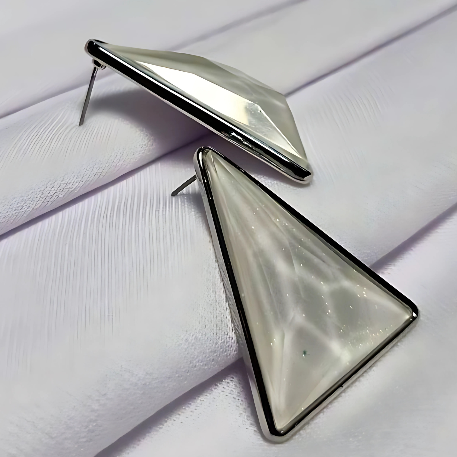 Triangular earrings with a metallic finish on a textured white surface