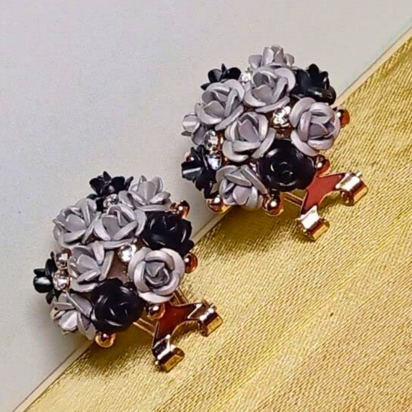 Pair of floral earrings with black, white, and gold colors on a textured surface.