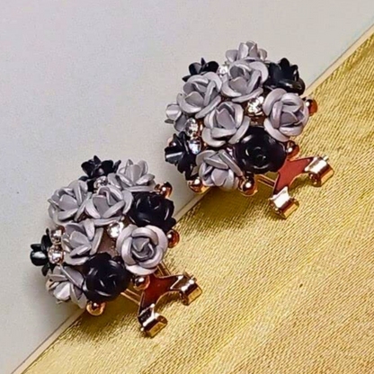 Pair of floral earrings with black, white, and gold colors on a textured surface.