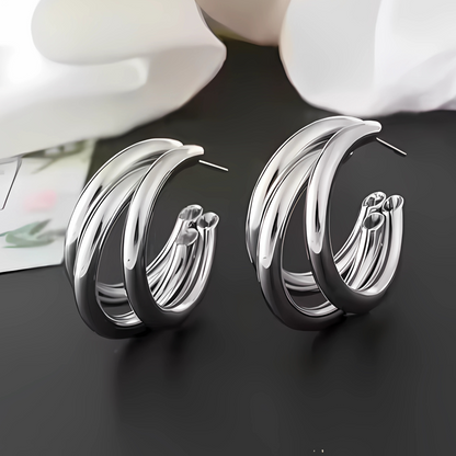Silver hoop earrings on a dark surface with white flowers in the background