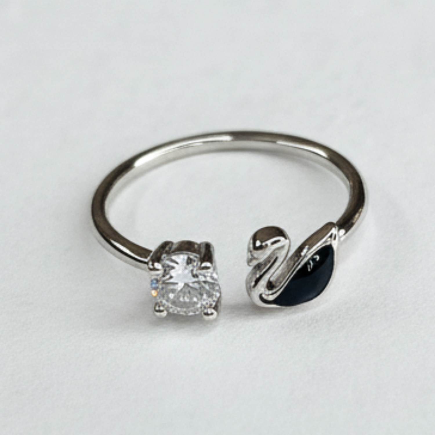 Silver ring with diamond and swan design on a light gray background
