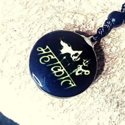 Black pendant with gold text and design on a sandy background
