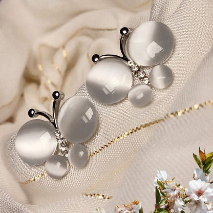 Silver butterfly-shaped earring with white stones on a soft fabric background
