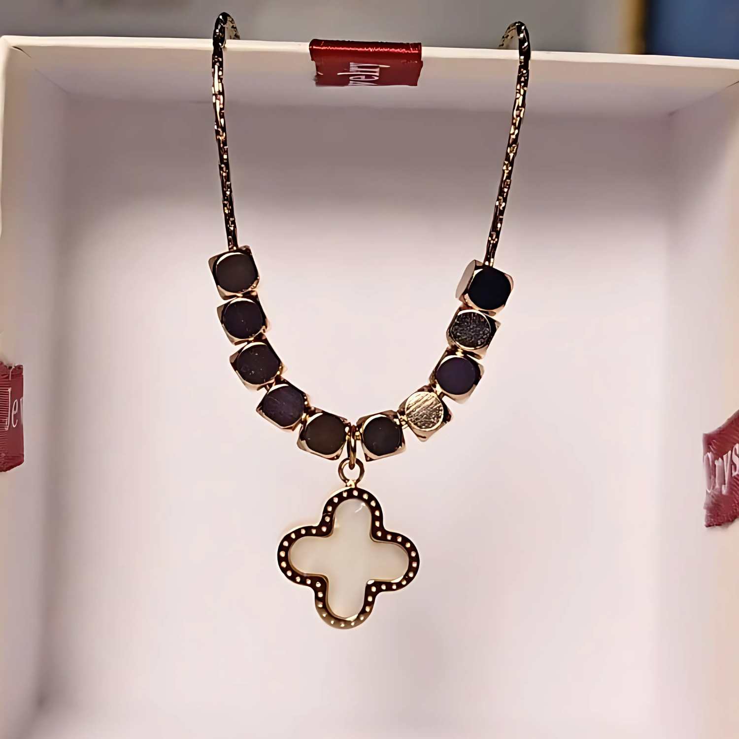 Necklace with gold beads and a clover-shaped pendant on a white background