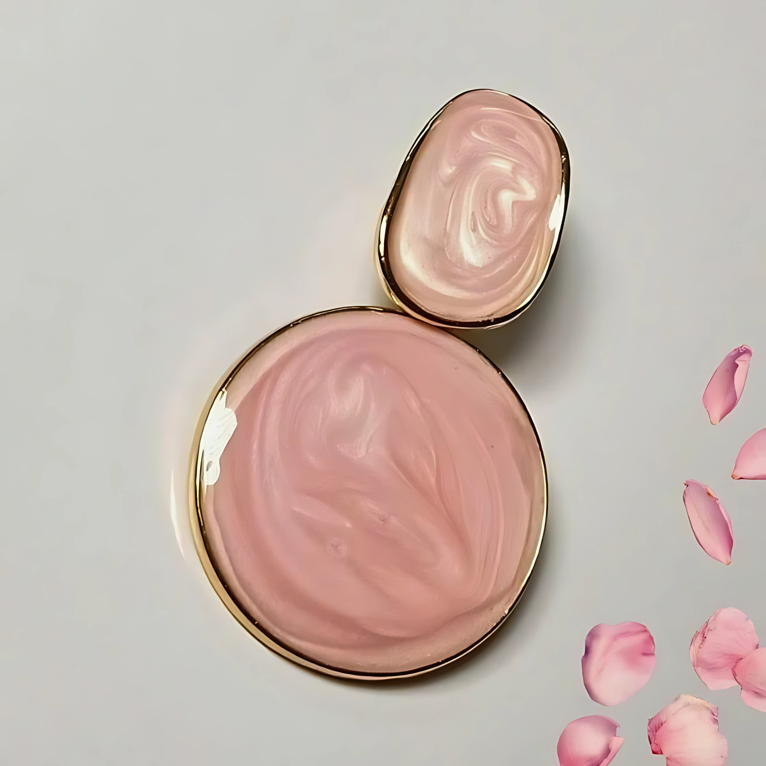 Pink earrings with gold accents on a light gray background with pink petals.