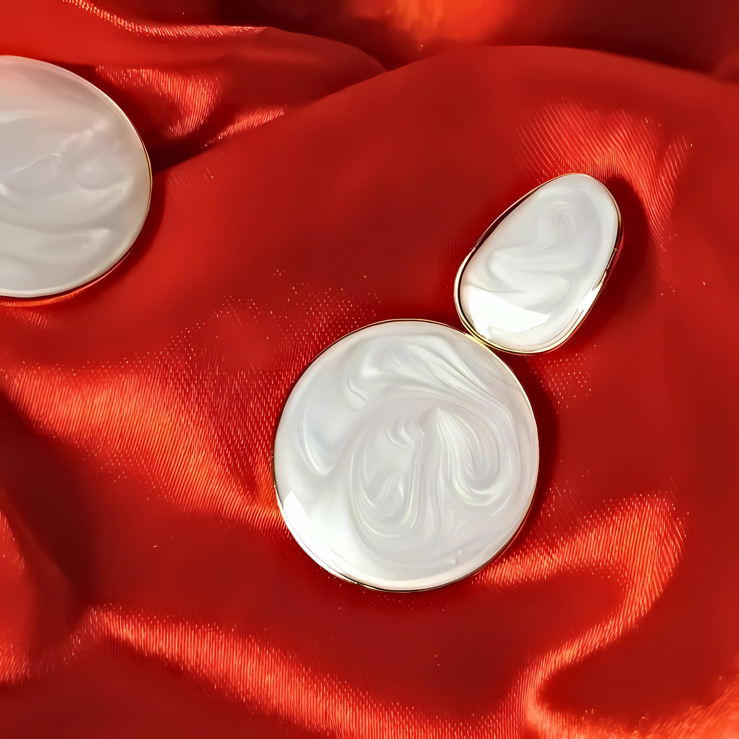 Two white marbled round objects with gold edges on a red fabric background