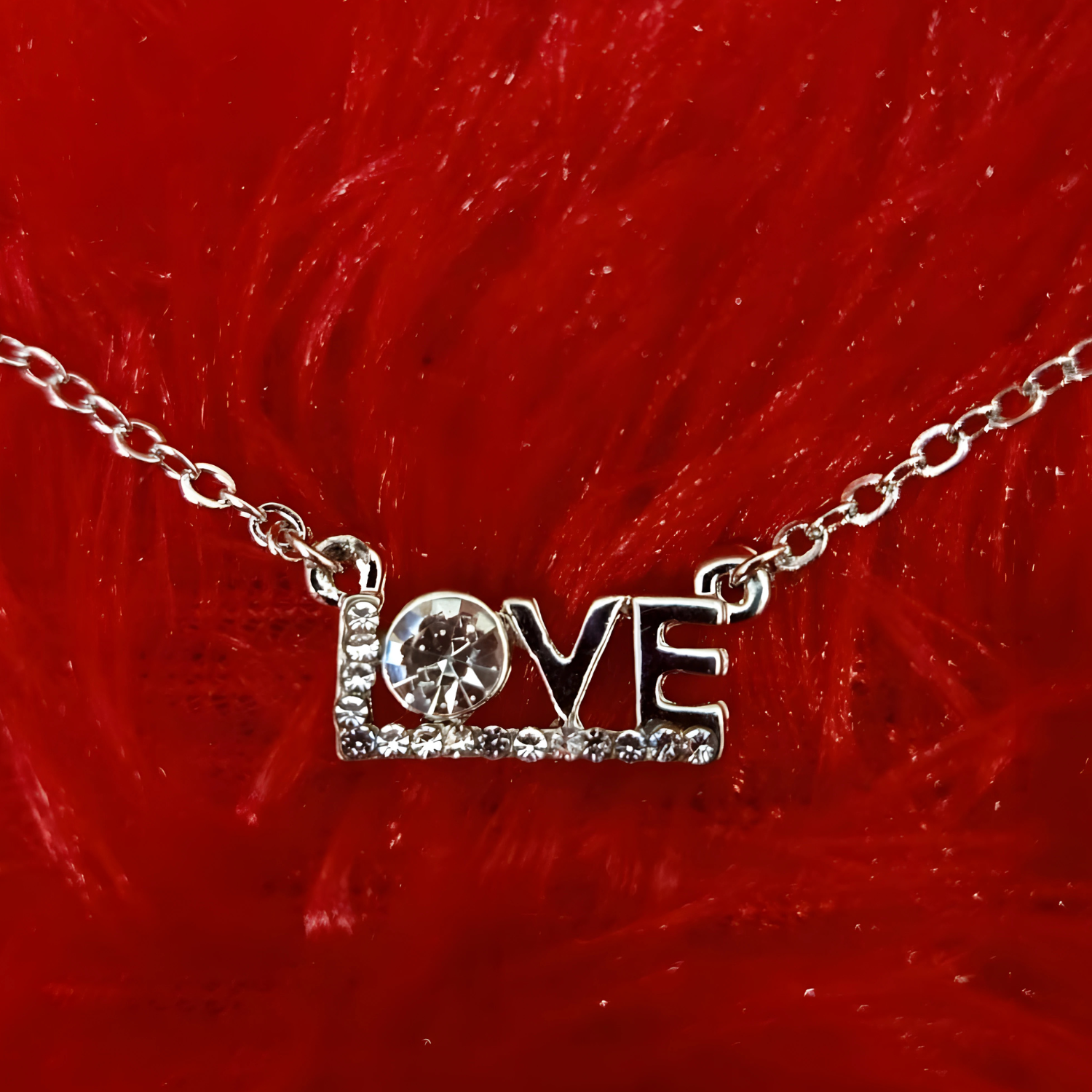 Silver 'LOVE' necklace with a small round pendant on a red furry background